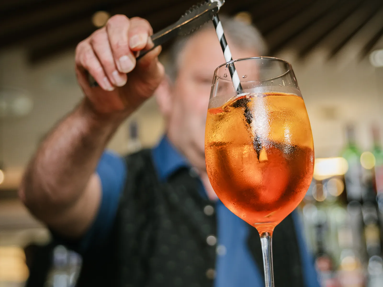 Bartender preparing Aperol Spritz with ice cubes and straw