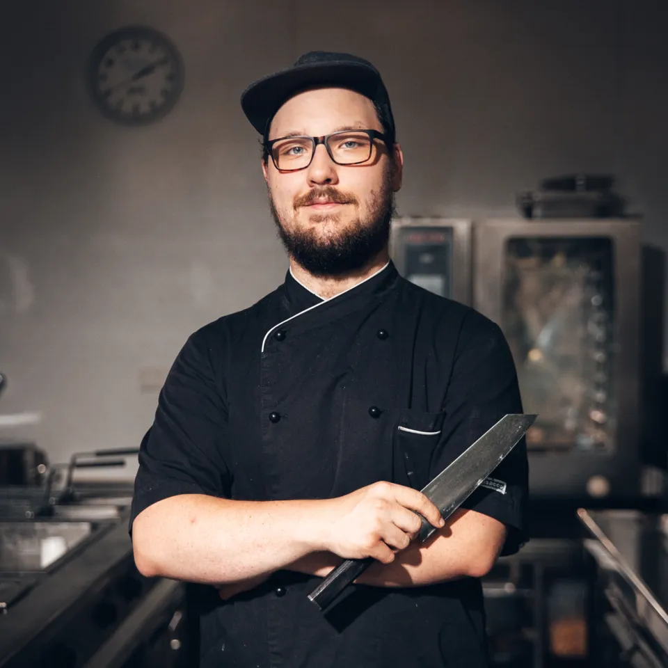 Chef in black uniform with knife in front of stainless steel kitchen