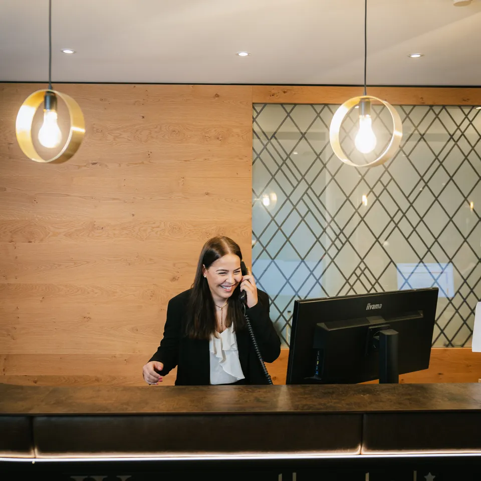 Woman at reception talking on the phone, wood paneling and modern lamps in the background