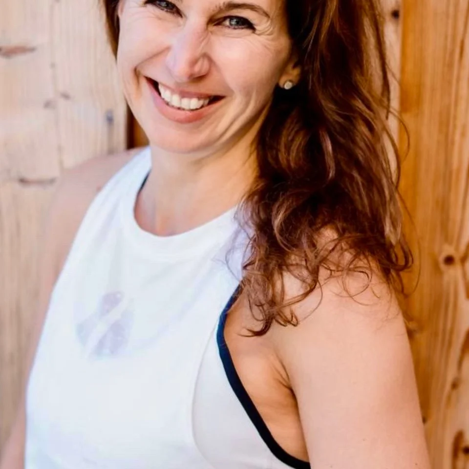 Lächelnde Frau in weißem Sporttop vor Holzwand