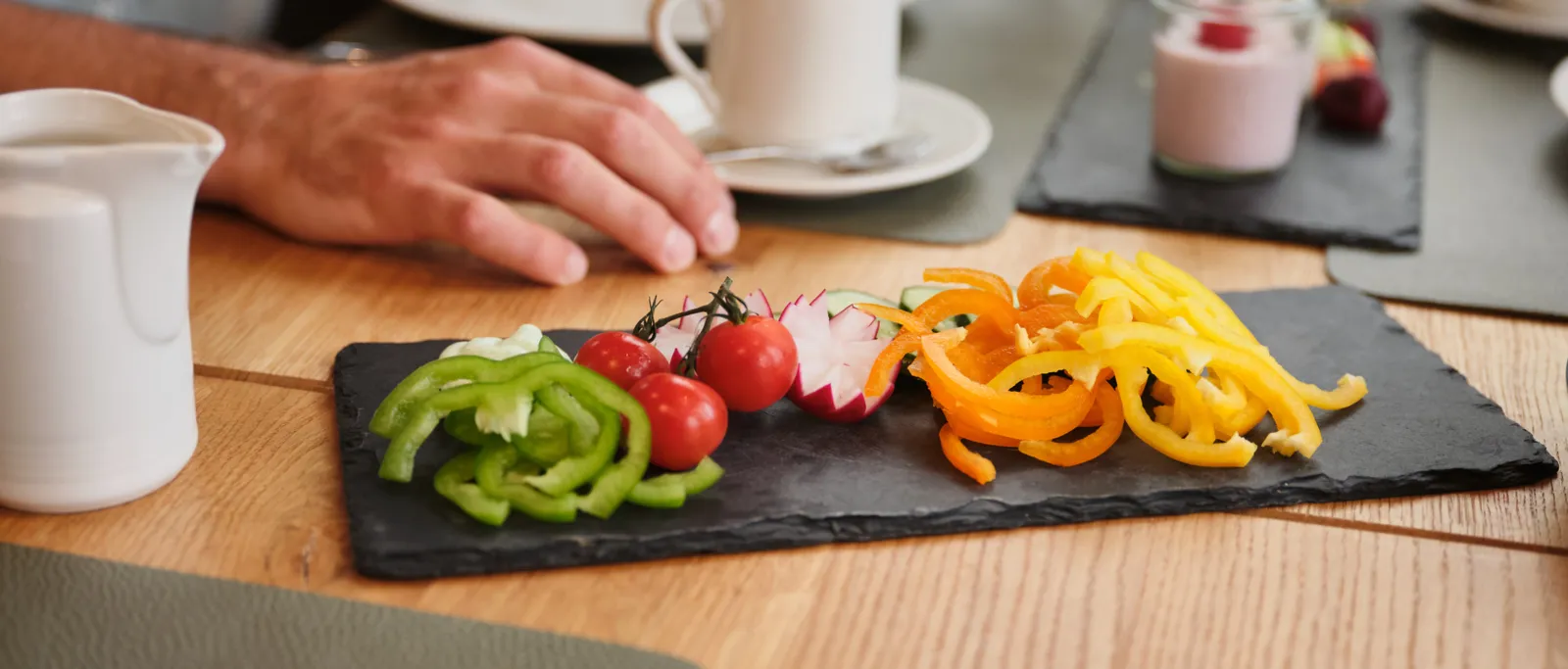 Vegetable platter with peppers, tomatoes and radishes next to cup and hand on table