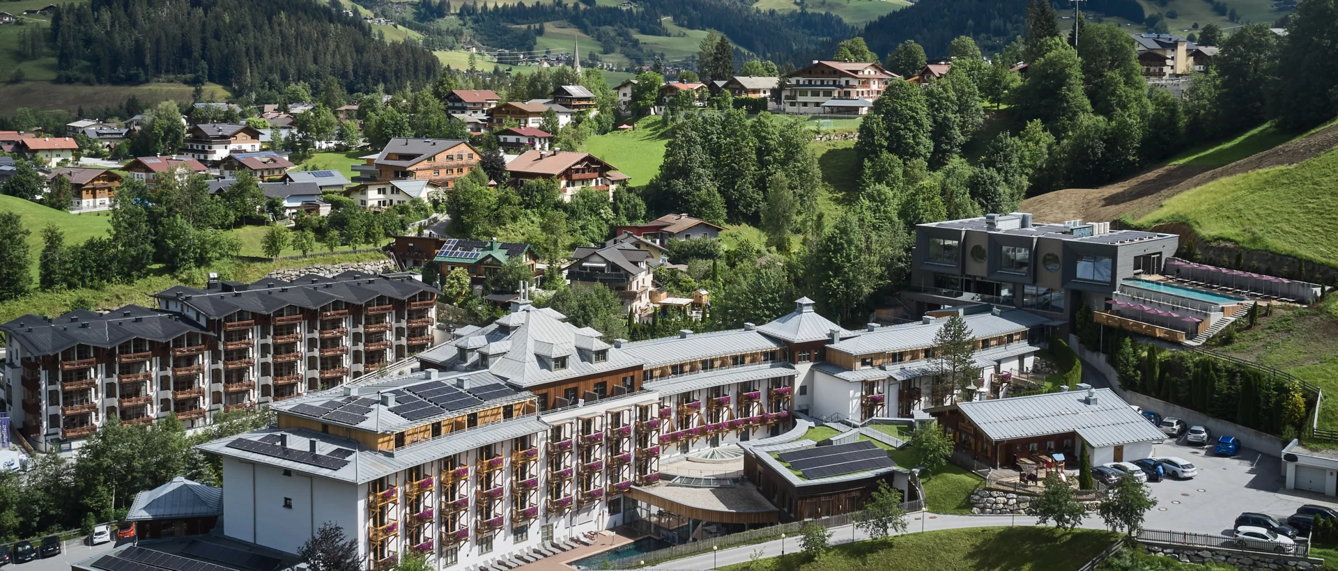 Aerial view of Sporthotel Wagrain in front of green hills under blue sky with clouds