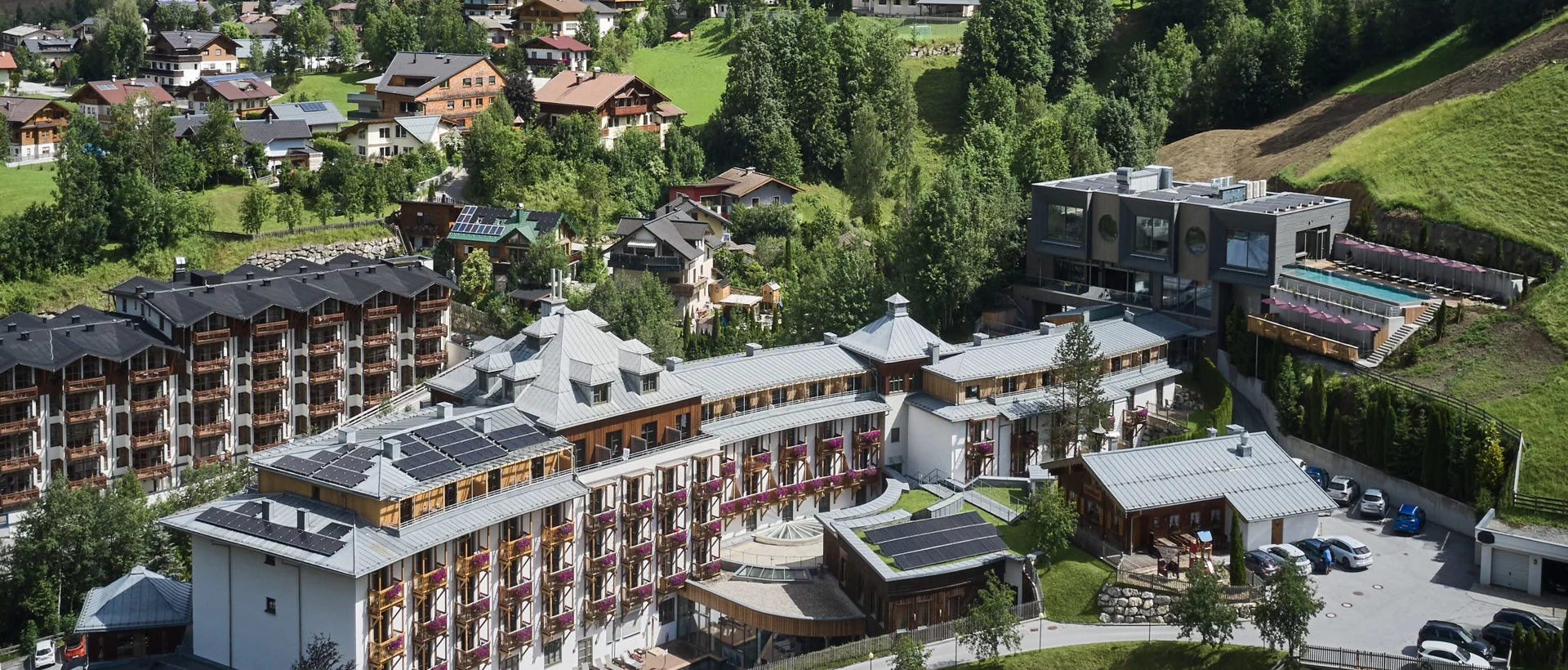 Luftaufnahme von Sporthotel Wagrain vor grüner Hügellandschaft unter blauem Himmel mit Wolken
