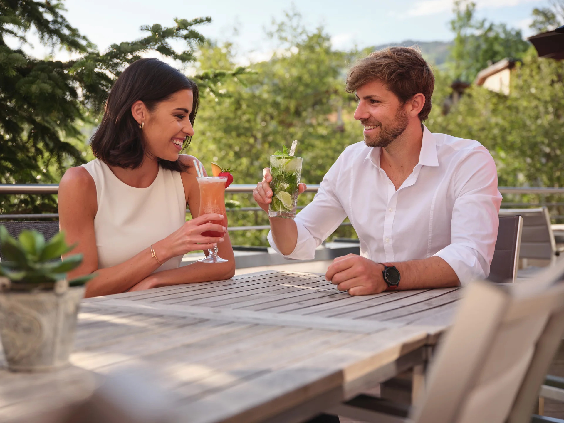 Couple toasting each other with cocktails on a wooden terrace