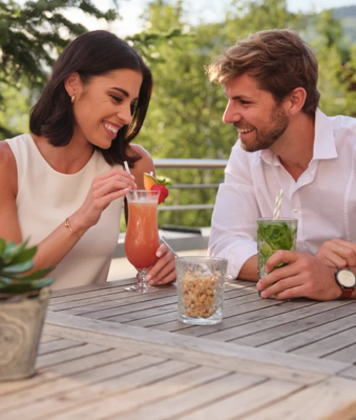 Frau und Mann sitzen mit Cocktails an einem Holztisch im Freien