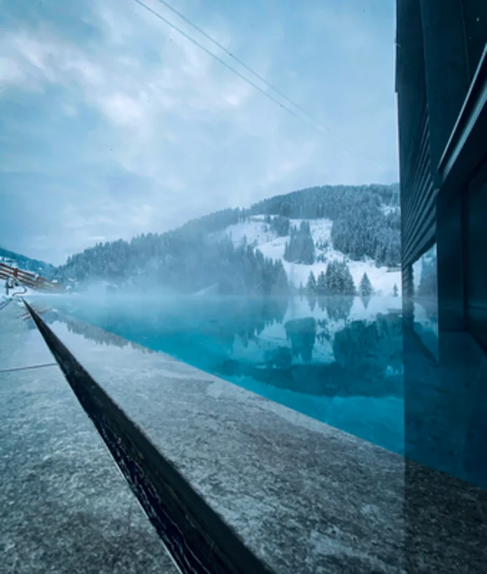 Türkisblauer Pool vor verschneiter Berglandschaft an einem trüben Wintertag