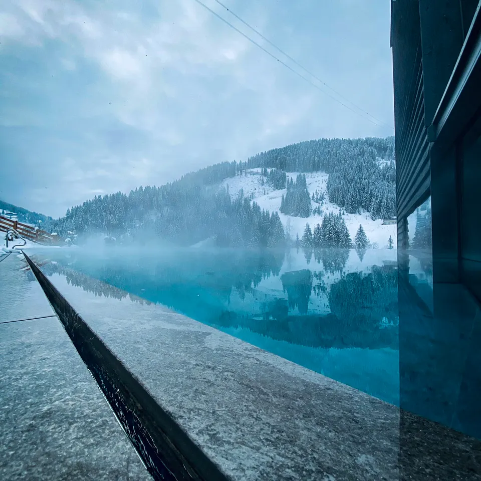 Türkisblauer Pool vor verschneiter Berglandschaft an einem trüben Wintertag