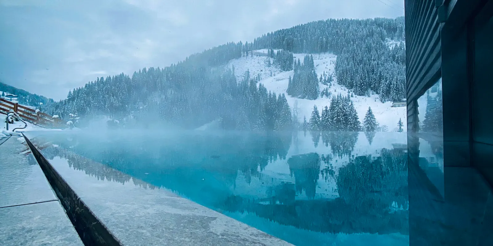 Turquoise pool in front of a snowy mountain landscape on a cloudy winter day