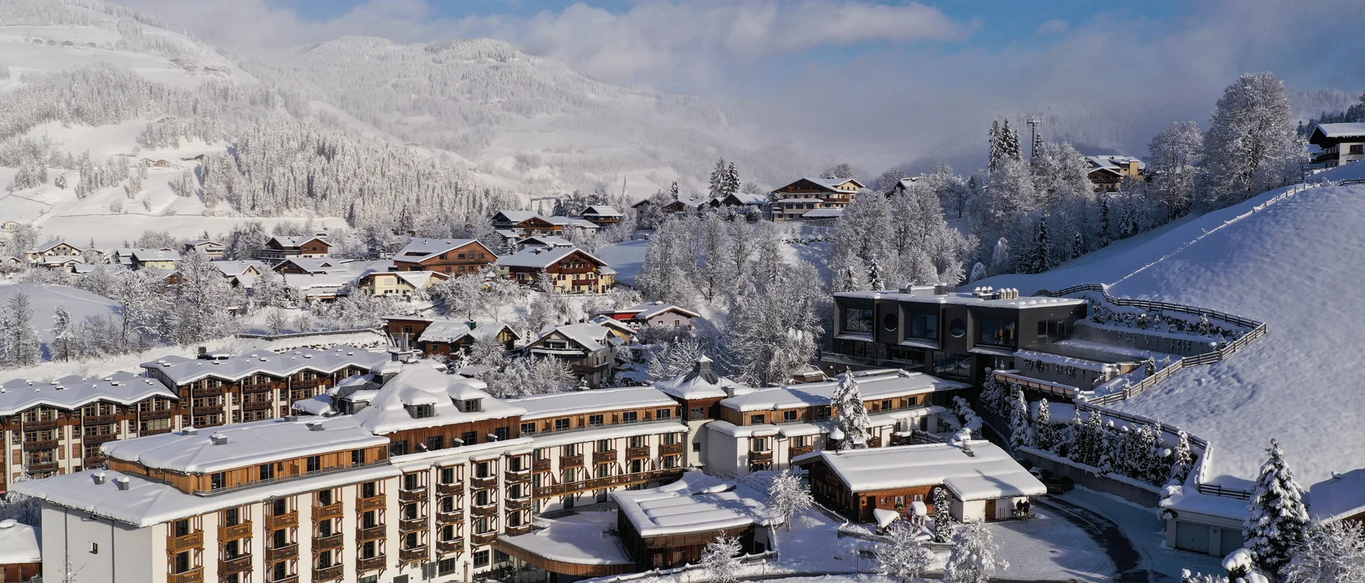 Winterliche Berglandschaft mit schneebedeckten Häusern und Bäumen unter blauem Himmel