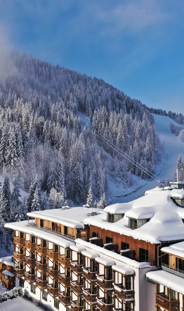Sporthotel Wagrain im Schnee vor bewaldetem Berg unter blauem Himmel