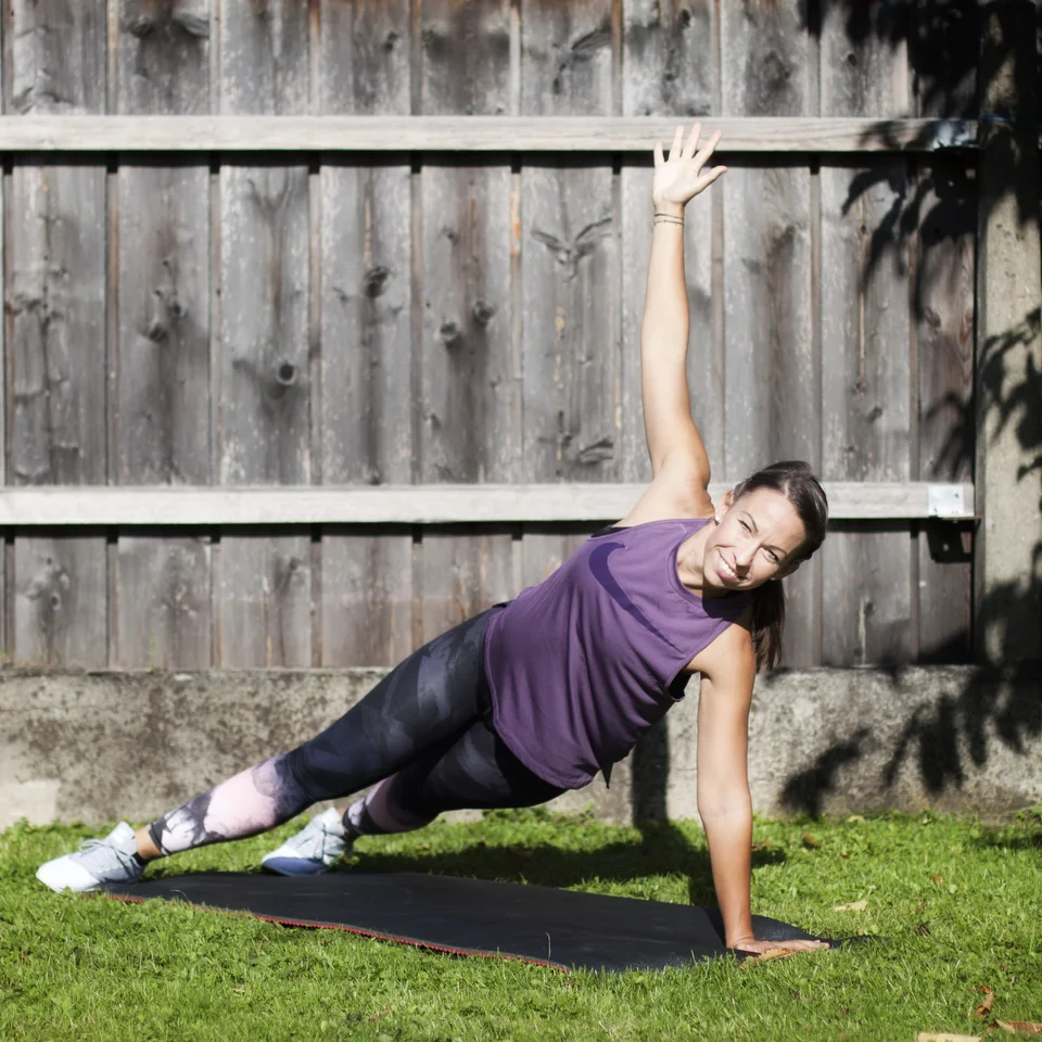Woman doing side forearm plank on a mat in the garden