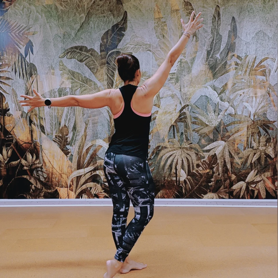 Woman in dance pose in front of tropical leaf wallpaper
