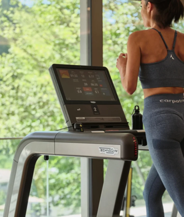 Woman running on treadmill in front of window with view of greenery