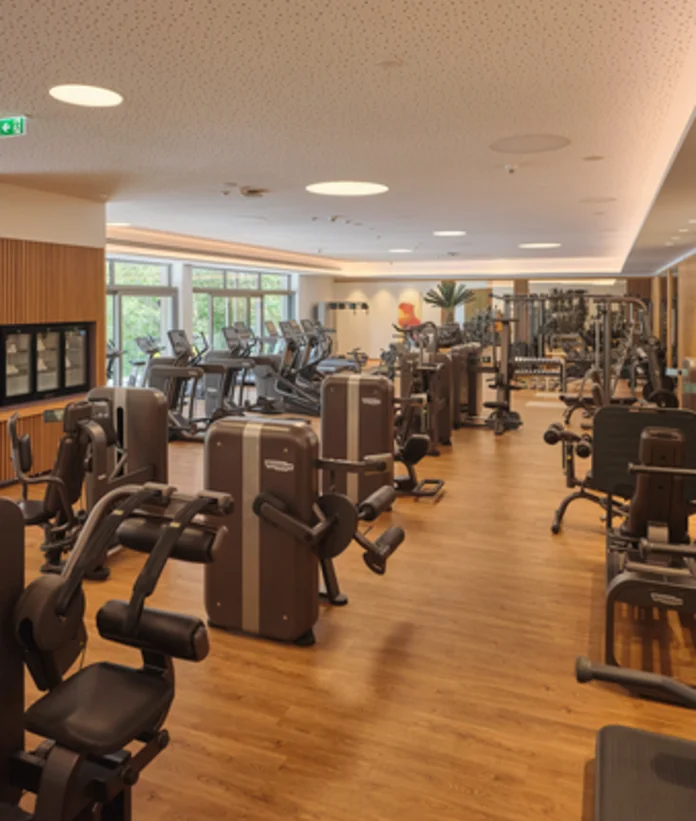 Heller Fitnessraum mit vielen Geräten und großen Fenstern
