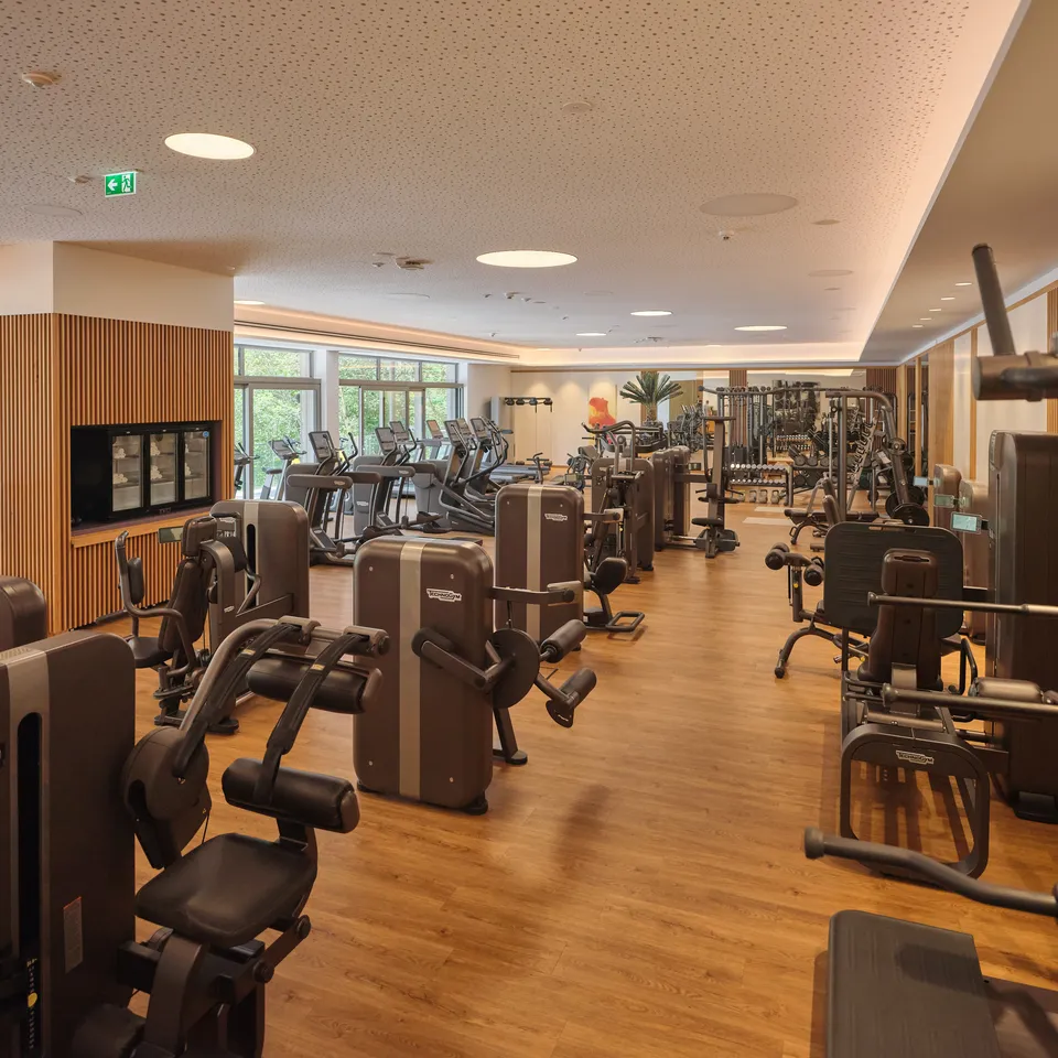 Heller Fitnessraum mit vielen Geräten und großen Fenstern
