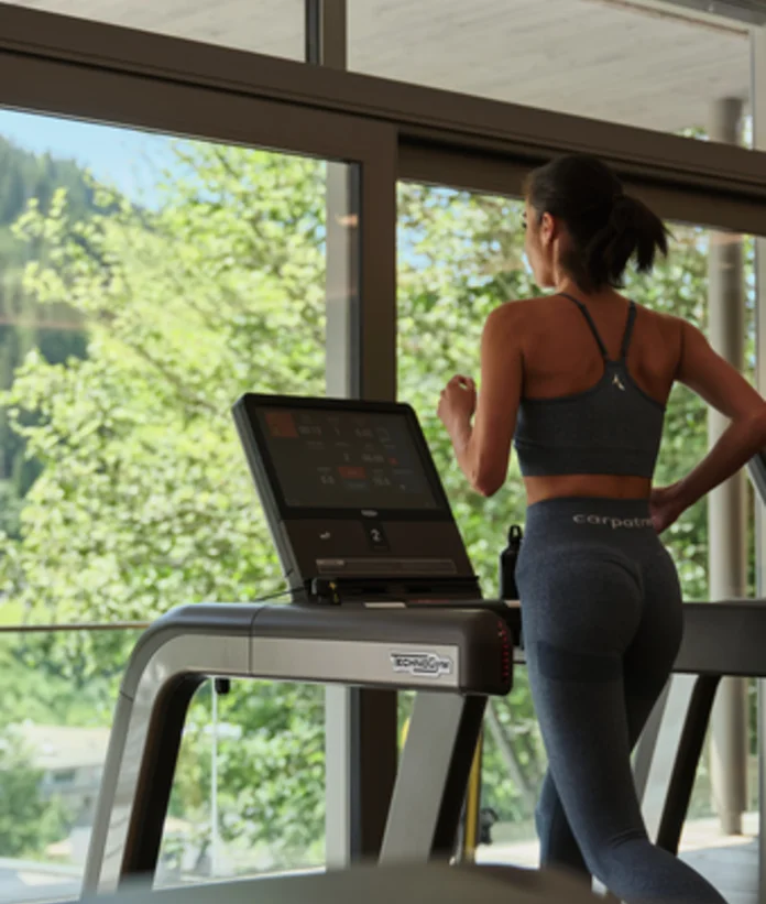 Frau trainiert auf Laufband vor Fenster mit Bergblick