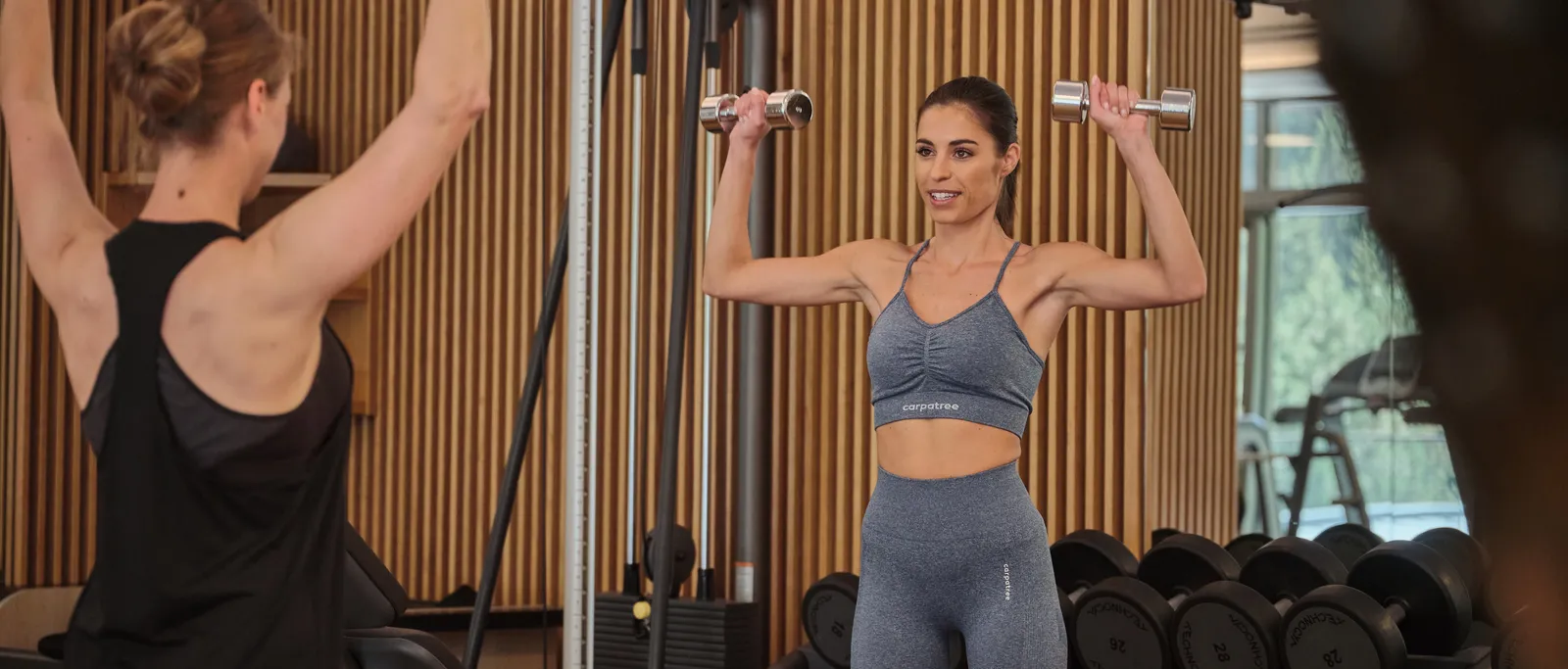 Woman training with dumbbells in the gym under the guidance of a trainer