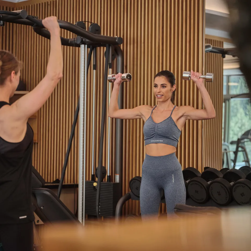 Frau trainiert mit Hanteln im Fitnessstudio unter Anleitung einer Trainerin
