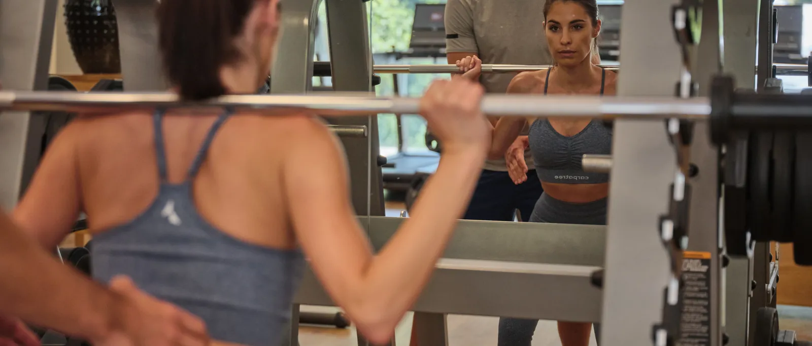 Woman training with barbell in gym, trainer gives assistance