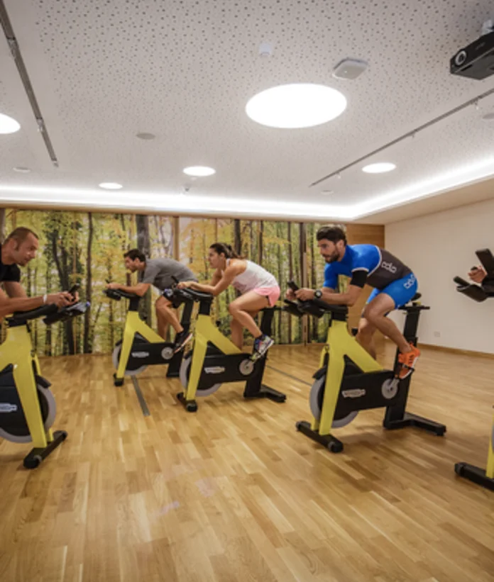 Fitnessraum mit mehreren Personen auf gelben Spinning-Rädern