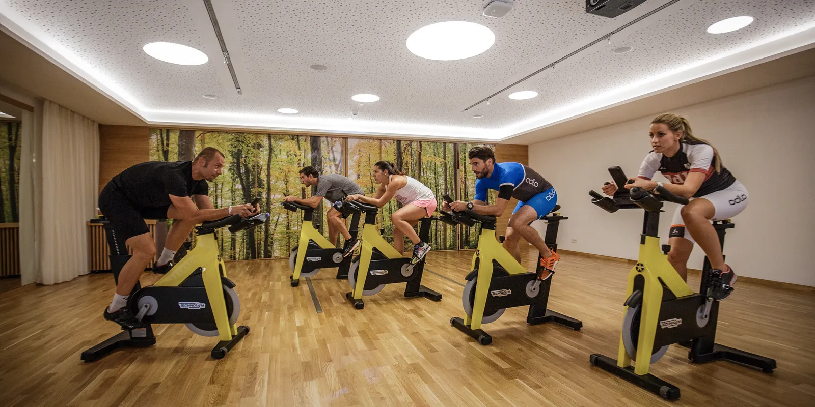 Fitnessraum mit mehreren Personen auf gelben Spinning-Rädern