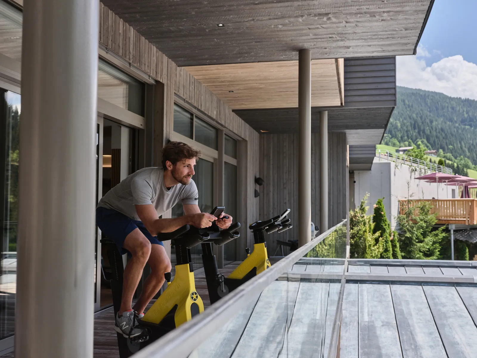 Mann trainiert auf Hometrainer auf Balkon mit Bergblick