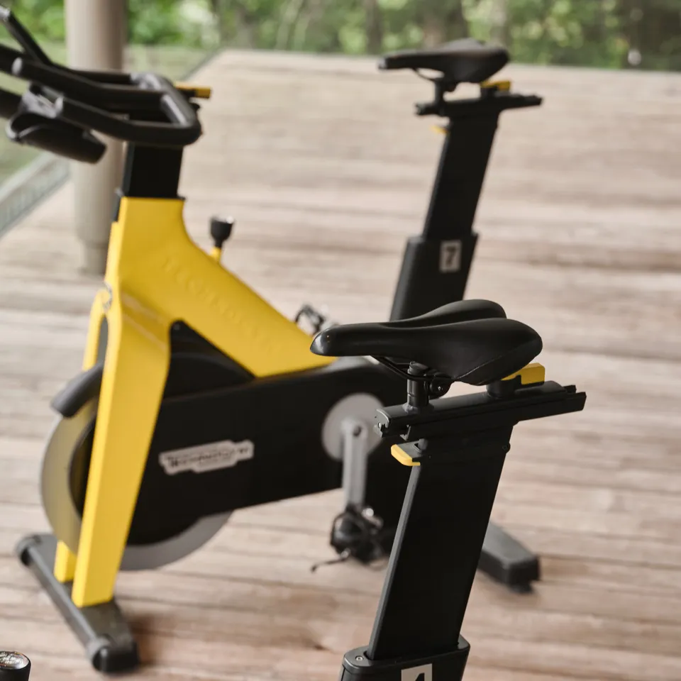 Zwei Indoor-Fahrräder, eines gelb, eines schwarz, in einem Fitnessraum