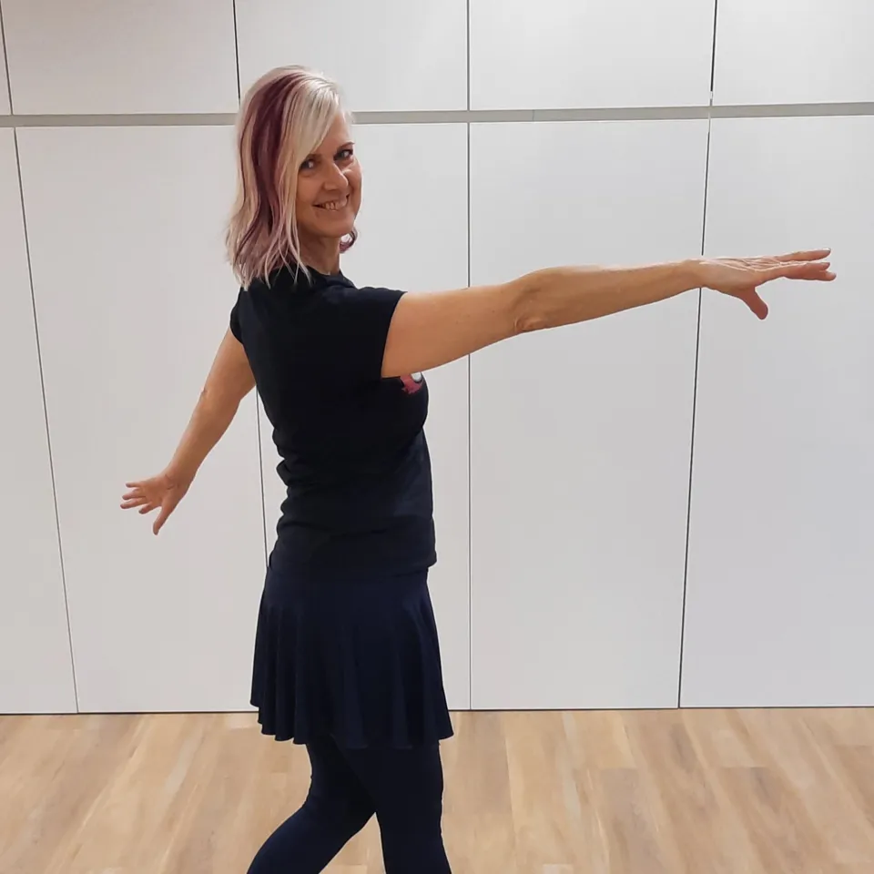 Woman in black dress and leggings dancing with outstretched arms