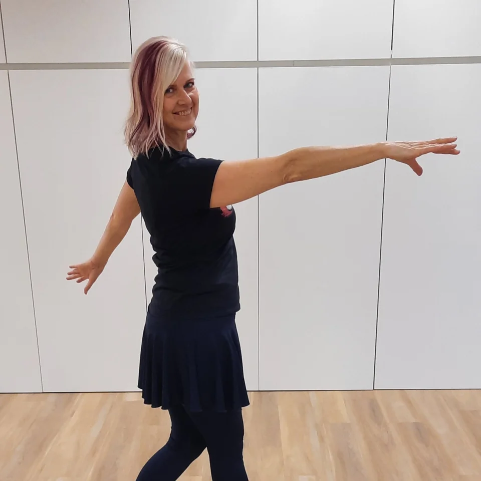 Frau in schwarzem Kleid und Leggings tanzt mit ausgestreckten Armen