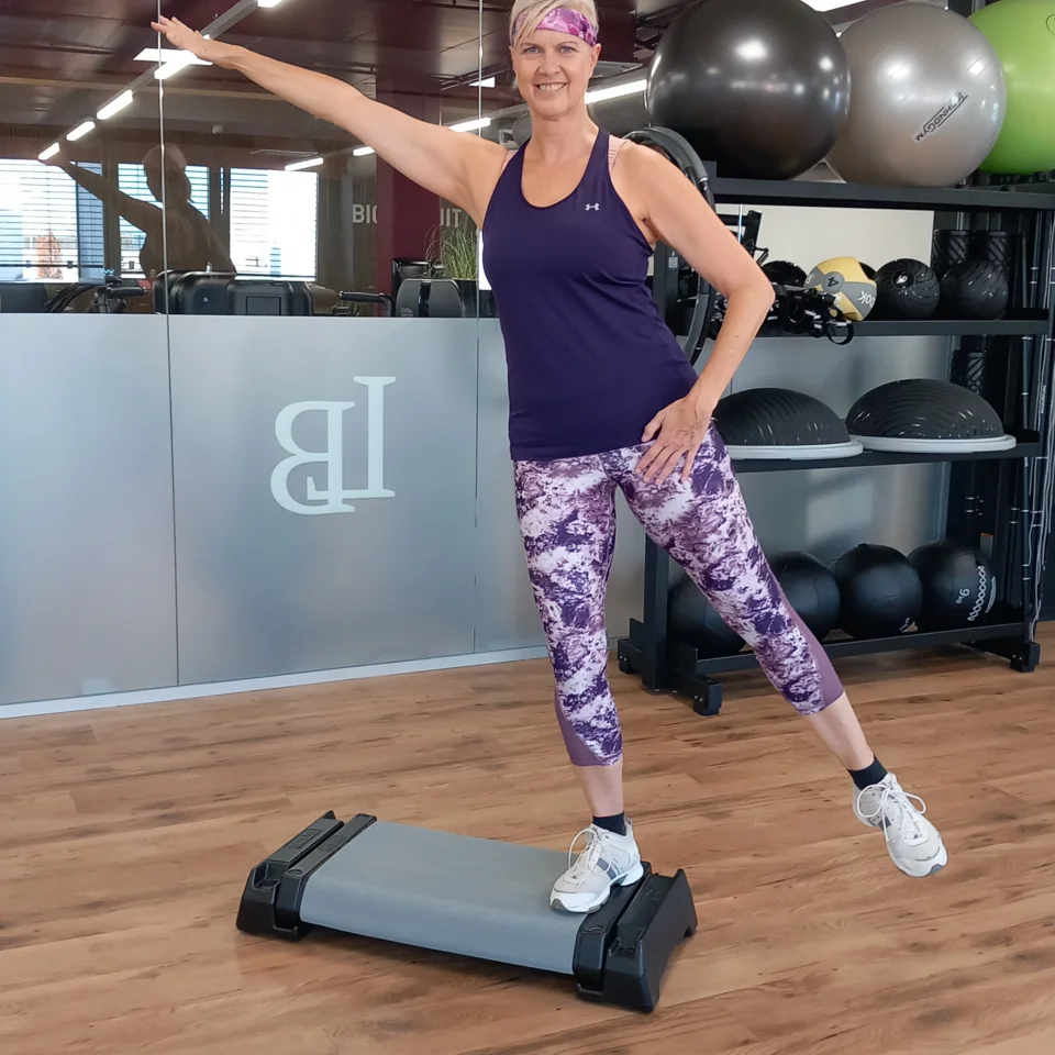 Frau mit Sportkleidung auf Stepper beim seitlichen Armheben im Fitnessstudio
