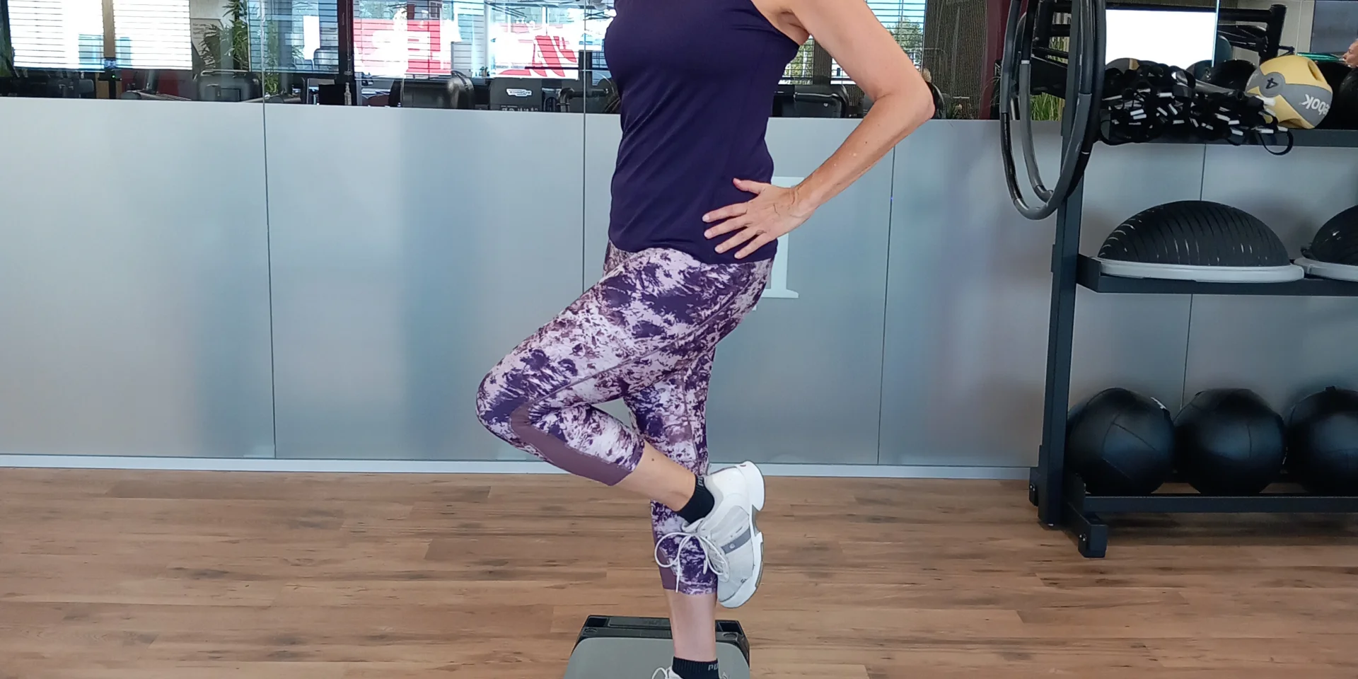 Frau auf Stepper im Fitnessstudio, Hand am Kopf, Bein angehoben