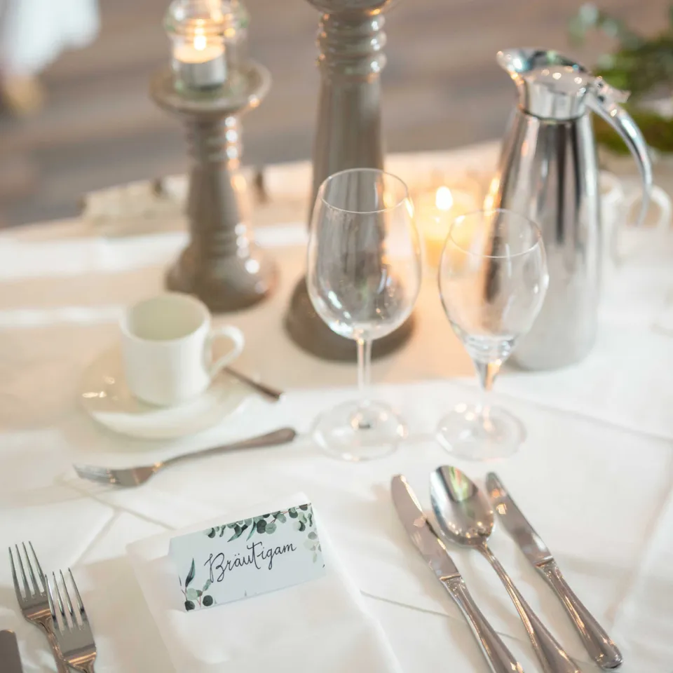 Gedeckter Hochzeitstisch mit Kerzenleuchtern, Gläsern, Besteck, Kaffeekanne und Namensschild