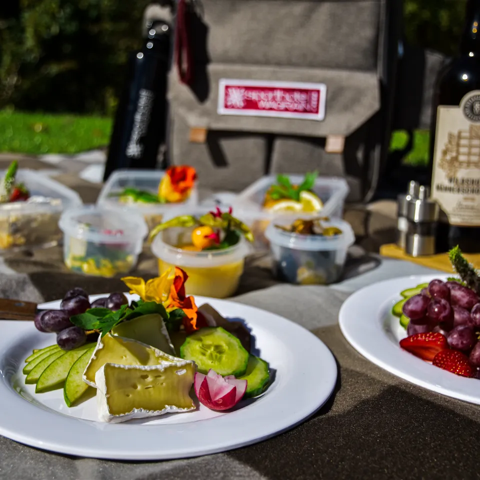 Picknick mit Käse, Obst, Gemüse, kleinen Behältern mit Speisen, Rucksack und Weinflaschen im Freien