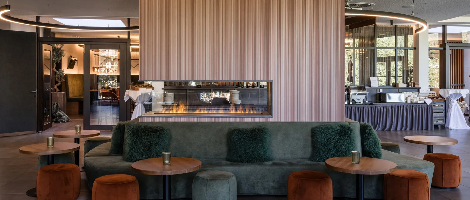 Lobby mit Sofa, Sesseln, Tischen und Kamin vor einer Wand mit Holzpaneelen
