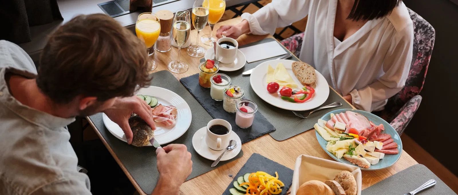 Couple having breakfast with sausage, cheese, yogurt, bread, coffee and juice at the table in the Sporthotel Wagrain
