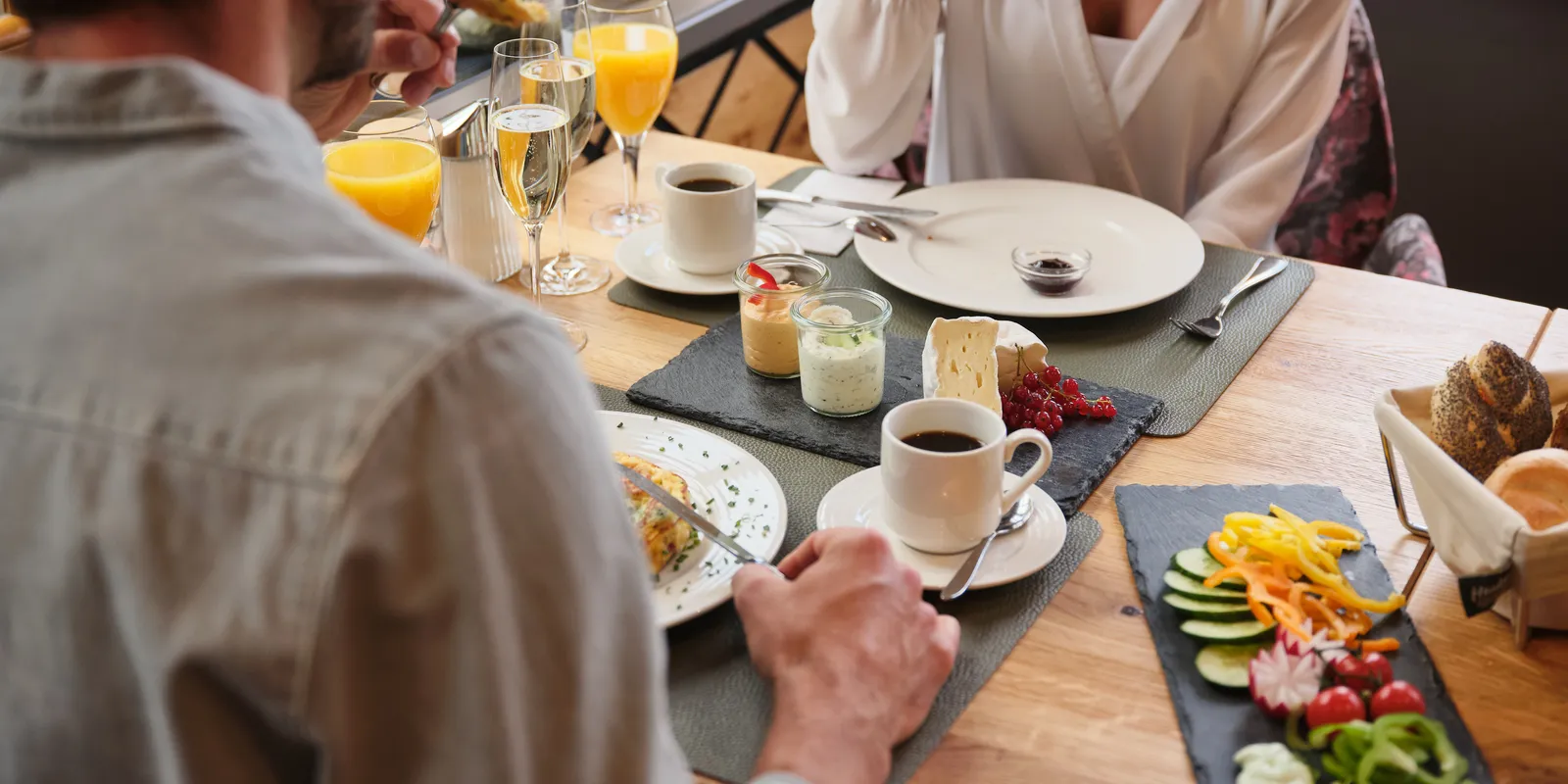 Paar beim Frühstück mit Saft, Kaffee, Brot und Aufschnitt am Tisch