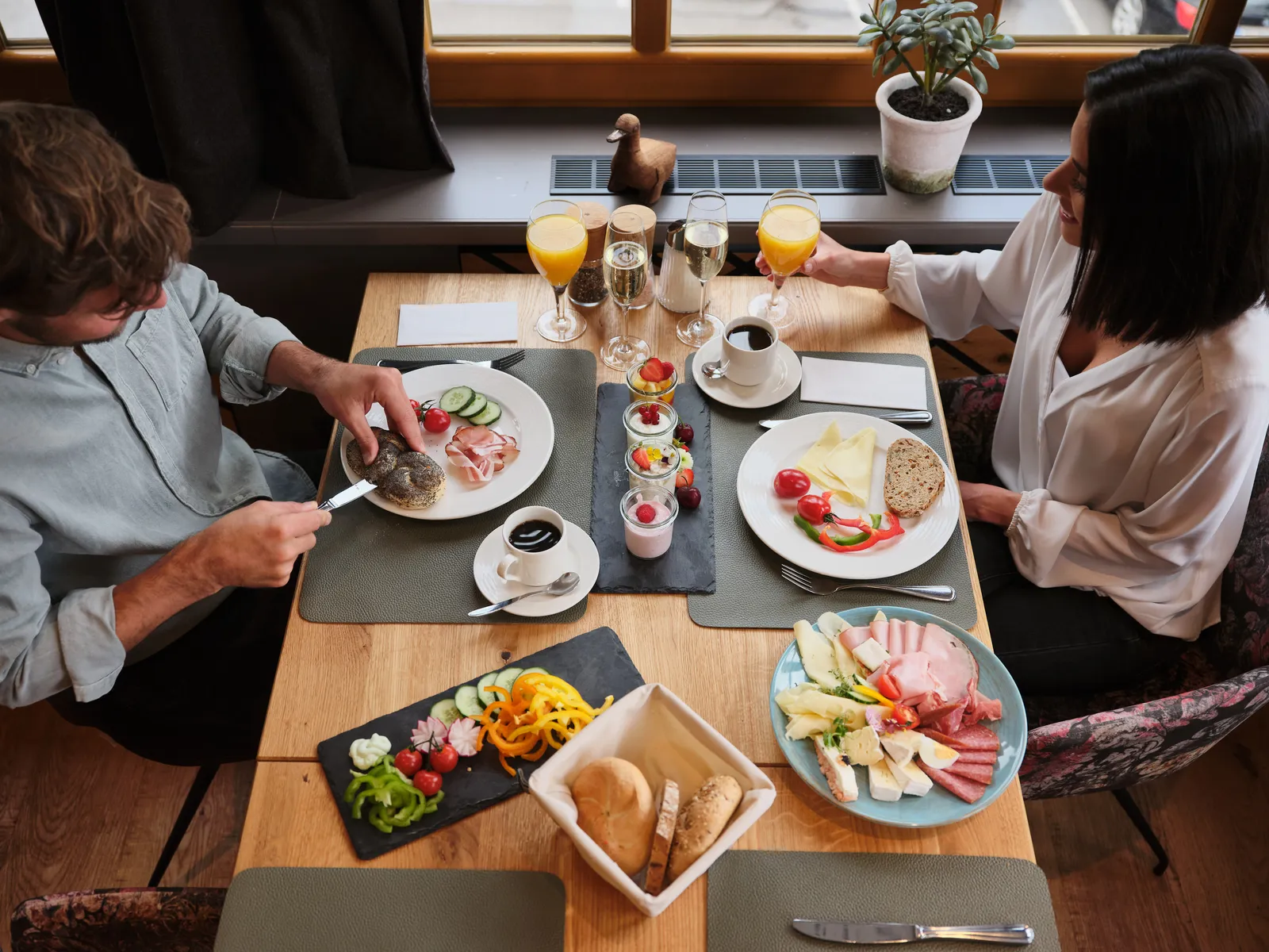 Set breakfast table with sausage, cheese, fruit, bread, coffee and orange juice for two people