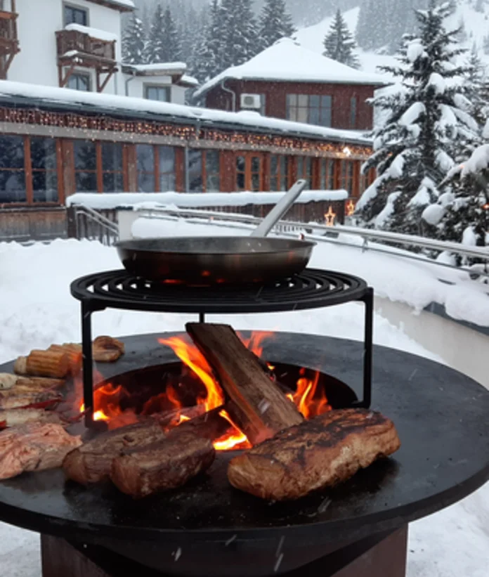 OFYR Grill mit Fleisch, Gemüse und Pfanne im Schnee vor Gebäuden