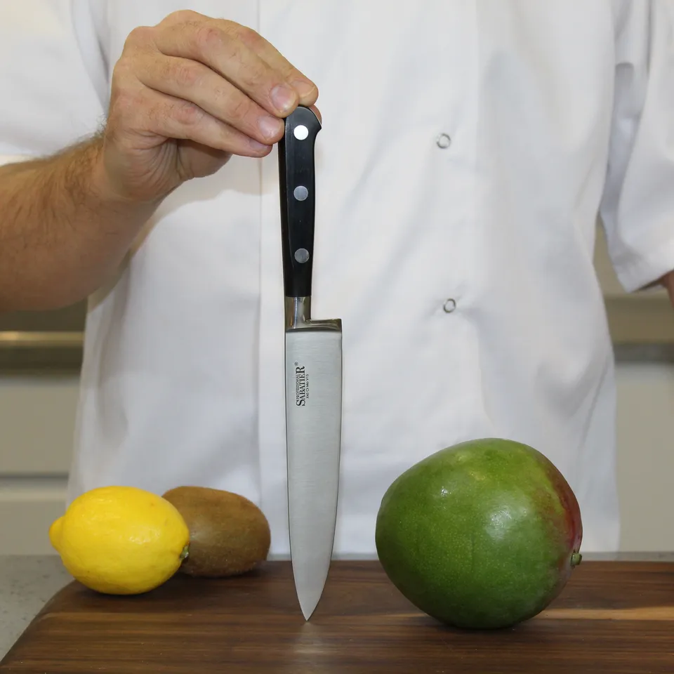 Koch hält Messer über Zitrone, Kiwi und Mango auf einem Holzbrett