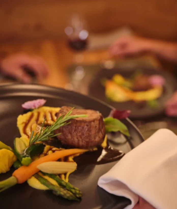 Angerichtetes Fleischgericht mit Gemüse auf dunklem Teller im Restaurant