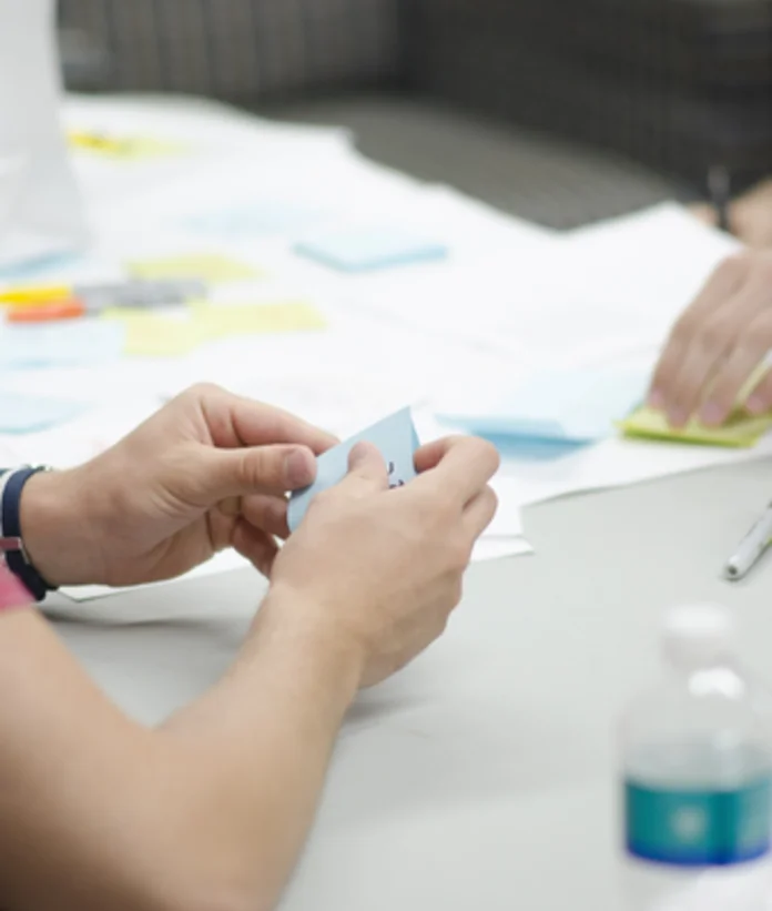 Person folding paper at table with notes and water bottle