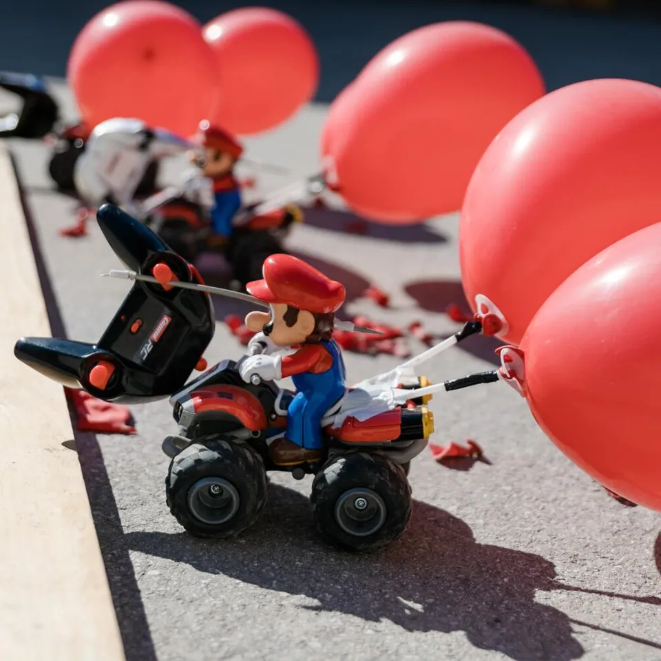 Mario-Figur auf Quad mit roten Ballons, Konfetti auf Asphalt