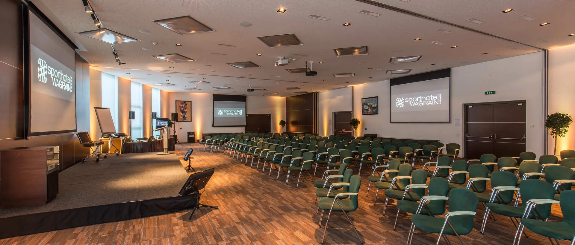 Seminar room with stage, screens and green chairs at the Sporthotel Wagrain