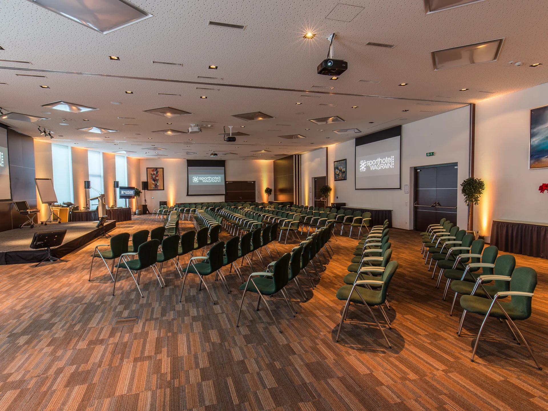Seminarraum mit Stuhlreihen, Leinwänden und Bühne im Sporthotel Wagrain