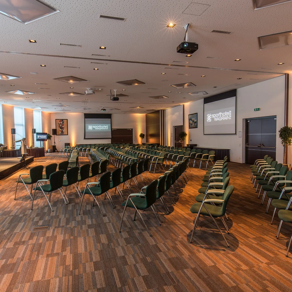 Seminarraum mit Stuhlreihen, Leinwänden und Bühne im Sporthotel Wagrain