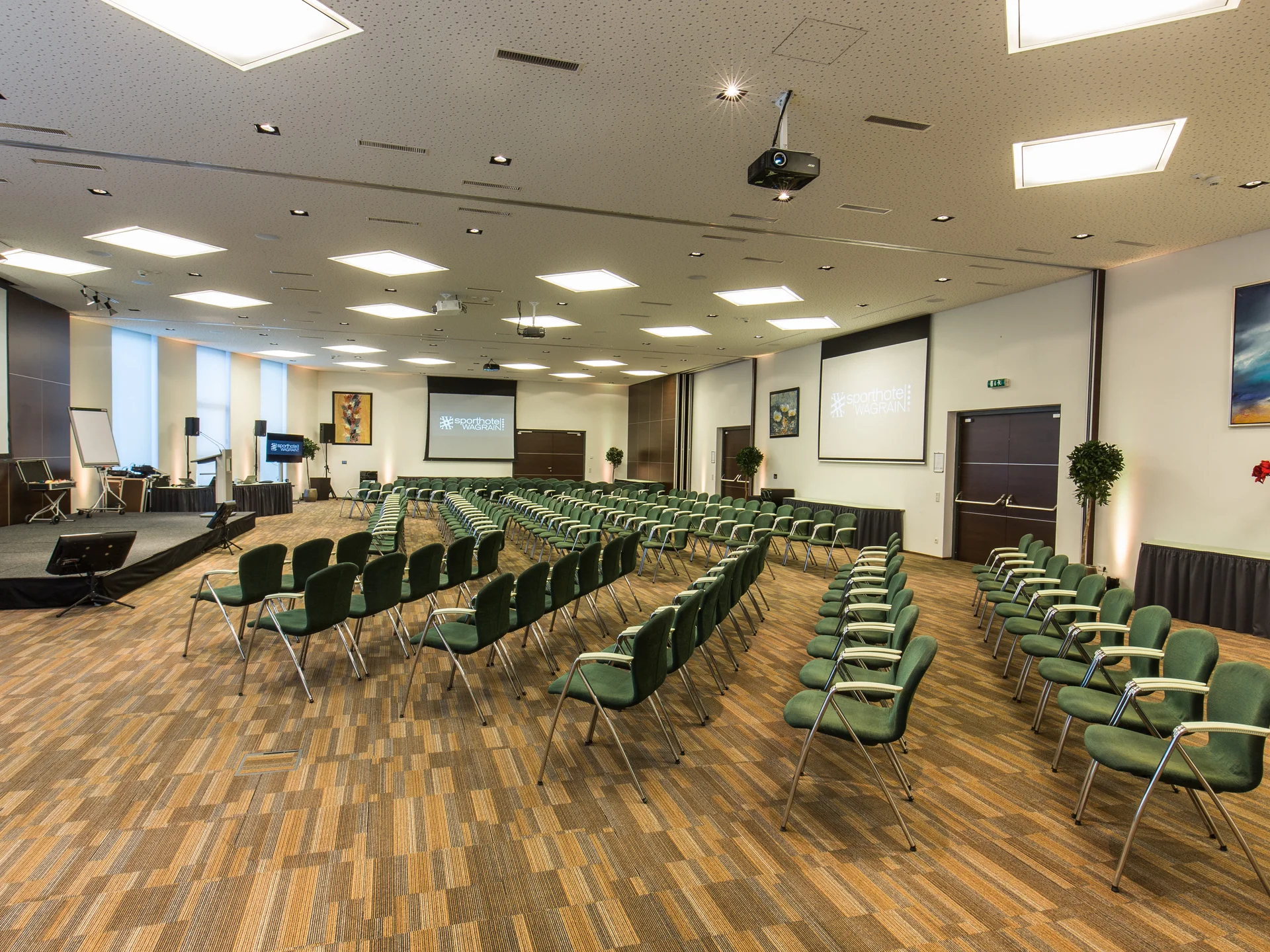 Seminarraum mit Stuhlreihen, Bühne und Projektoren im Sporthotel Wagrain