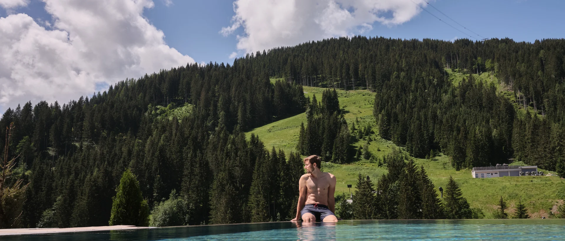 Frau sitzt am Pool mit Blick auf bewaldeten Berghang