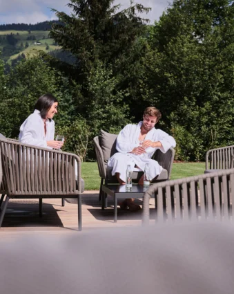 Two people in bathrobes sitting on a terrace overlooking green hills