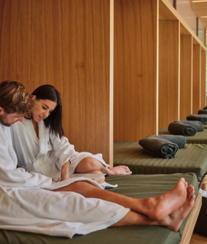 Couple in bathrobes relaxing on loungers in the wellness area with wooden walls