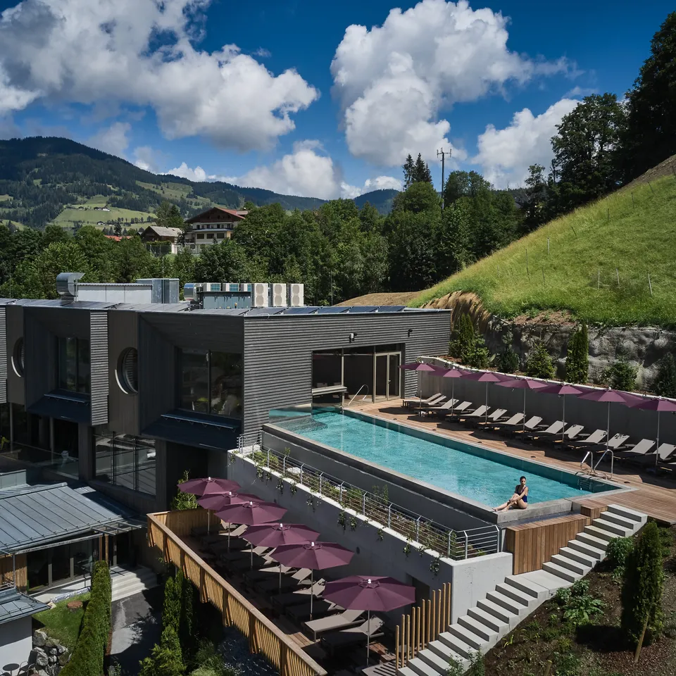 Sporthotel Wagrain mit Pool auf Dachterrasse, Liegen und Blick auf grüne Hügel unter blauem Himmel